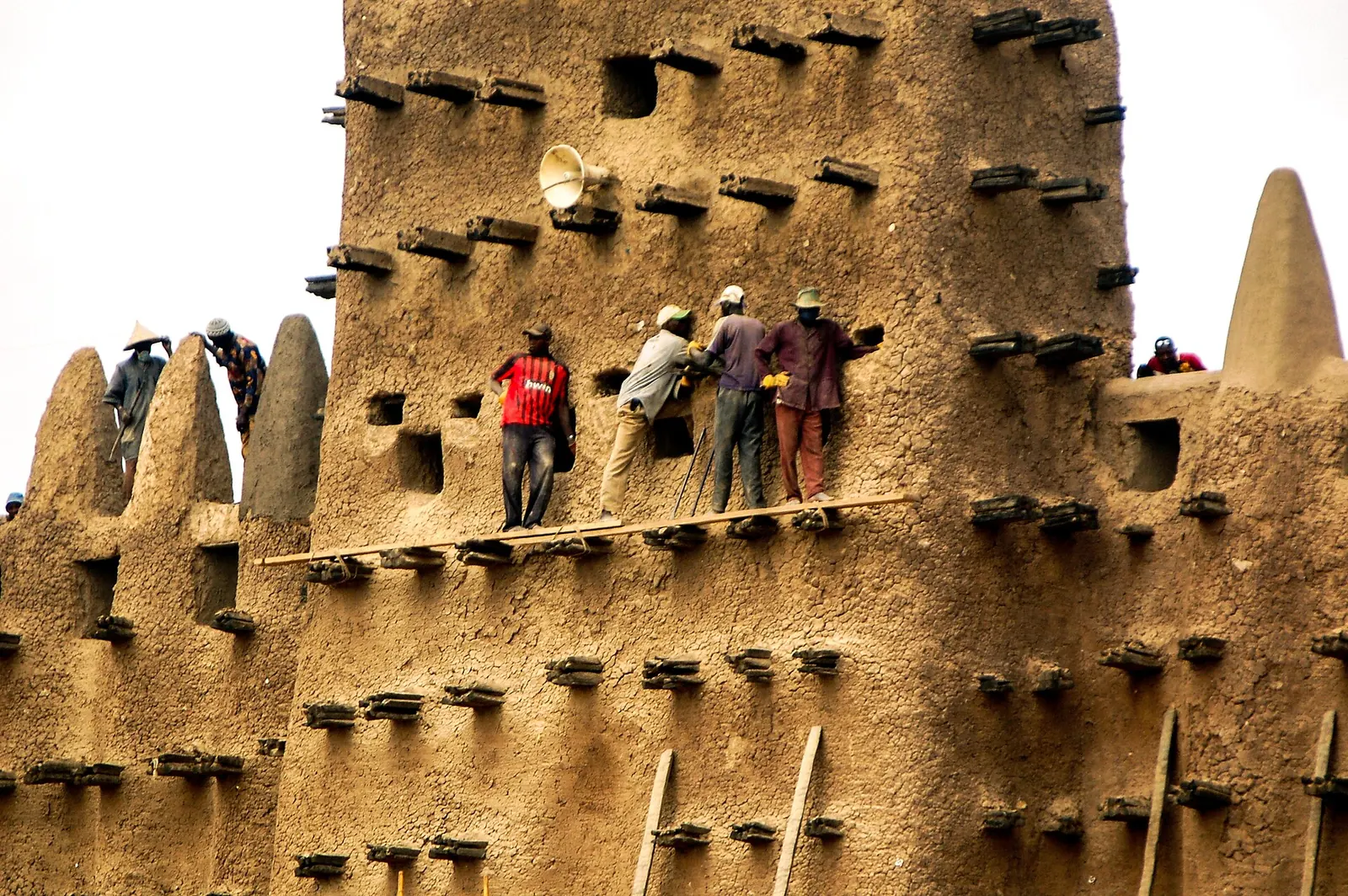 Men standing on a plank laid across the palm-stick toron of a mud-brick tower, spreading fresh plaster