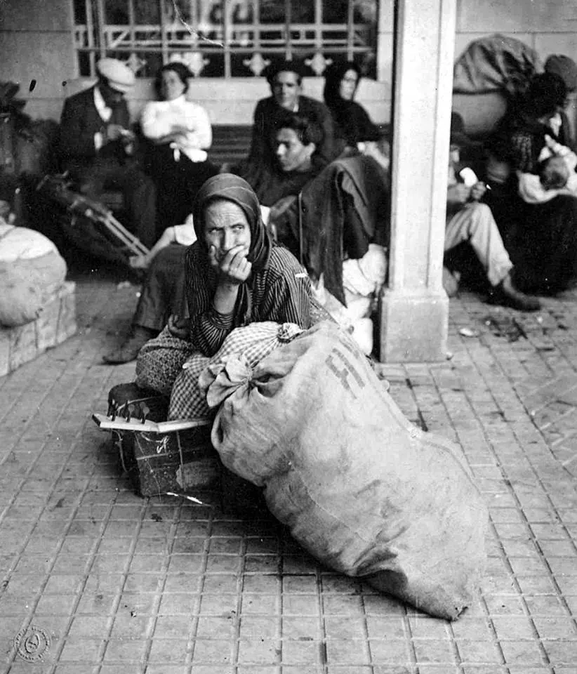 Black and white photograph of a woman seated on a large sack among other new arrivals