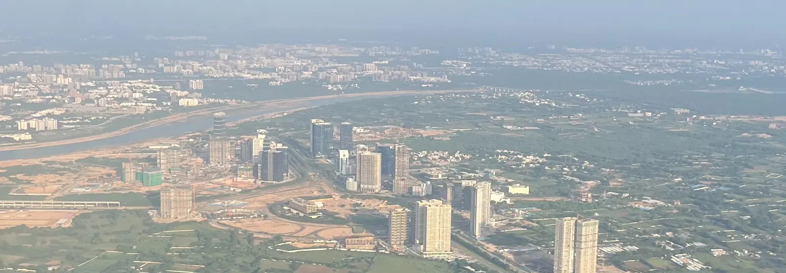 Aerial view of glass towers and construction sites beside a river, with farmland around them
